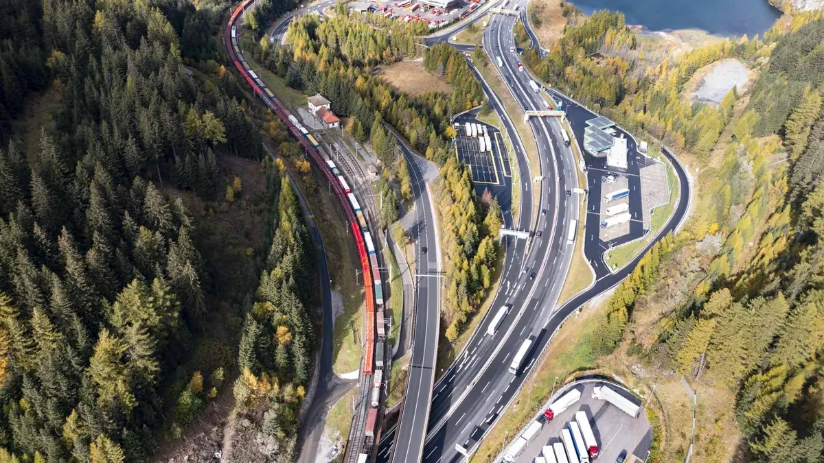 Aerial view of freight trains and motorway traffic sharing an Alpine valley