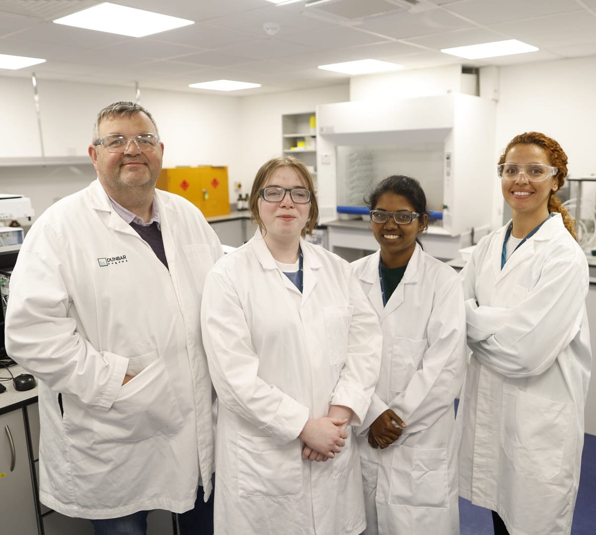 Four members of the Dunbar Pharma quality control team in white lab coats and safety glasses in a laboratory